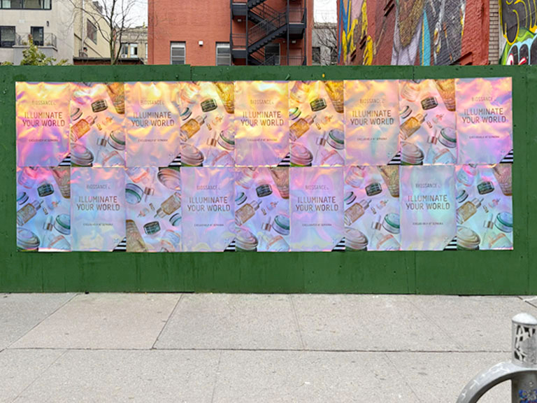 Biossance holographic posters installed on a green construction wall in Soho, New York City.