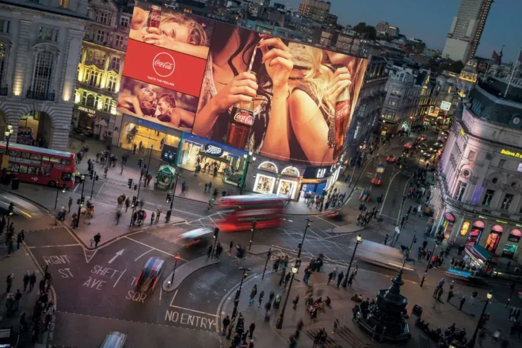 Coca-Cola billboard at Piccadilly Lights in London, featuring vibrant imagery of people enjoying drinks, surrounded by bustling streets and iconic architecture, symbolizing the cultural significance of outdoor advertising.