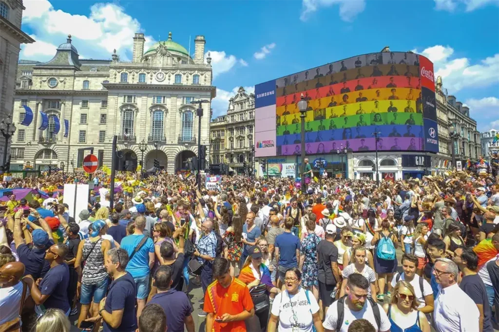 Crowd gathered at Piccadilly Circus with vibrant advertising display, showcasing colorful graphics and branding, during a lively event in London.