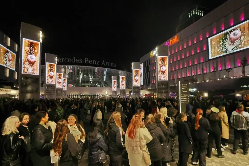 Crowd gathered outside the Mercedes-Benz Arena at night, featuring illuminated digital displays showcasing promotional content, emphasizing the importance of cultural relevance in global advertising.