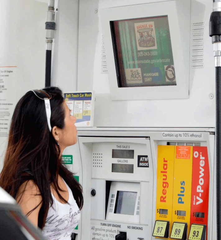 Woman interacting with a gas pump TV screen displaying advertisements, emphasizing gas pump advertising's effectiveness in engaging consumers.