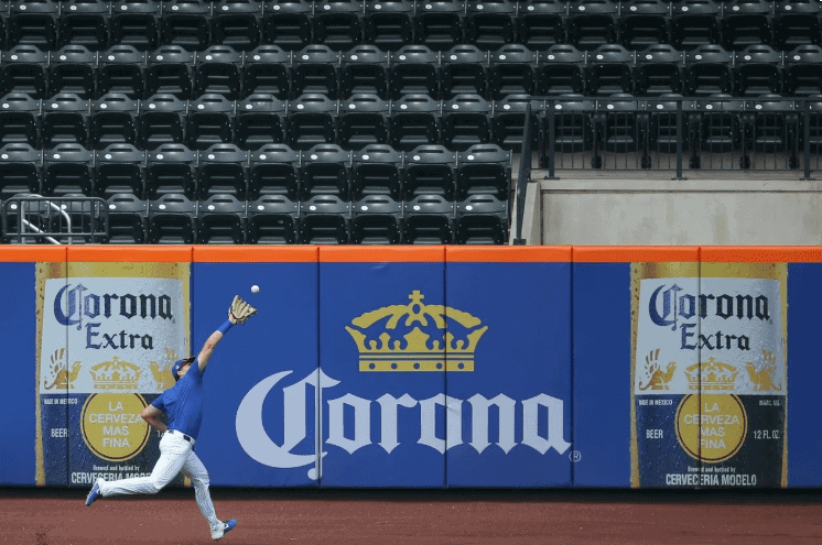 Baseball player catching a ball against a backdrop featuring prominent Corona Extra advertisements on the outfield wall, emphasizing sports advertising and brand visibility.
