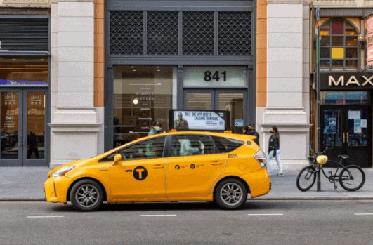 Yellow taxi parked on city street, showcasing potential for taxi trunk advertising to enhance brand visibility and awareness.