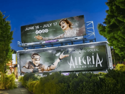 Billboard advertising for Cirque du Soleil's Alegría in Portland, featuring vibrant performers and event details for the expo center, showcasing innovative marketing strategies in a culturally rich urban setting.