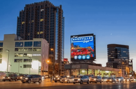 Billboard displaying "The Nashville Sign" in a bustling urban setting, showcasing vibrant advertising amidst city buildings and traffic, emphasizing Nashville's marketing potential.