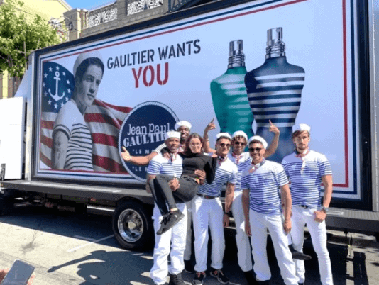 Group of brand ambassadors in sailor outfits posing in front of a promotional truck featuring Jean Paul Gaultier fragrance campaign, emphasizing field marketing engagement and brand visibility.