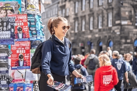Brand ambassador distributing promotional flyers in a bustling NYC street, showcasing guerrilla marketing strategies to engage consumers.