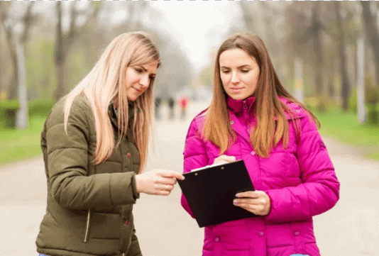 Two women discussing and reviewing a clipboard in a park, representing brand ambassadors engaged in marketing activities.