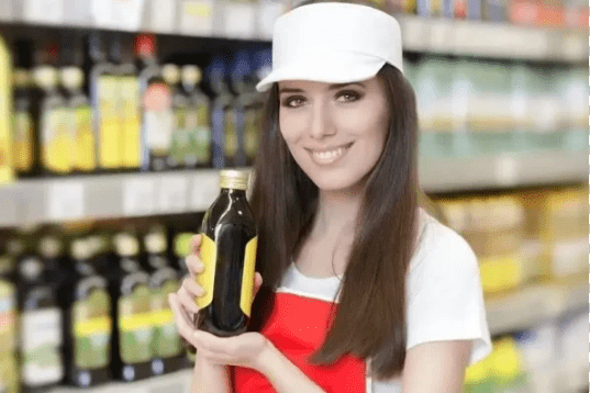 Smiling brand ambassador holding a product bottle in a grocery store aisle, promoting product sampling for increased brand awareness and customer engagement.