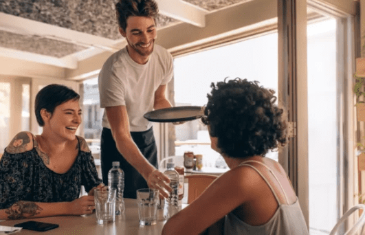 Waiter serving drinks to two smiling women.