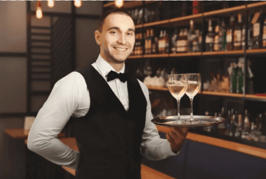 Professional bartender in a tuxedo holding a tray with two wine glasses, showcasing sophisticated bartending services for corporate events.