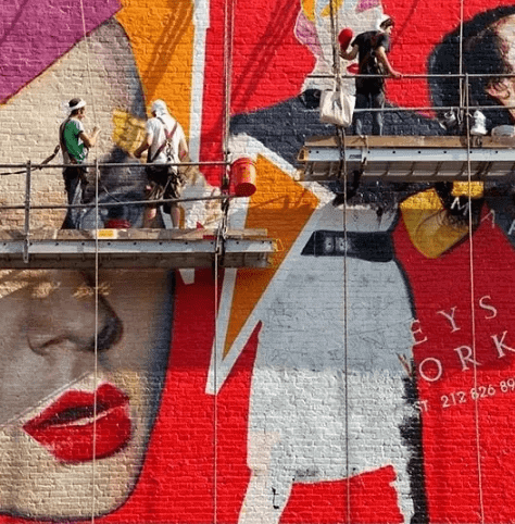 Mural artists painting a vibrant mural featuring bold colors and striking imagery, showcasing mural art as an innovative marketing strategy.