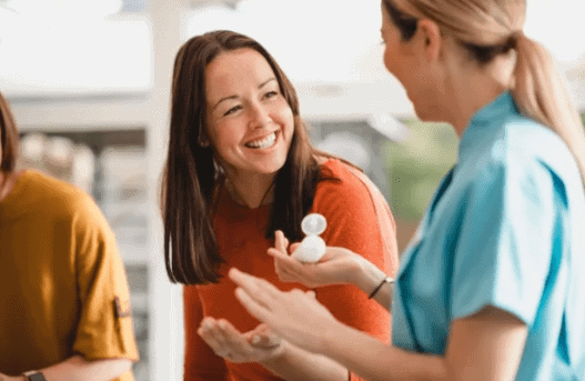 Two women engaging in a lively conversation, one smiling and gesturing with hands, the other wearing a blue shirt holding a small object, reflecting the importance of emotional connections in experiential marketing.