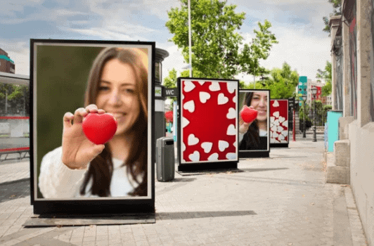 Billboard advertising featuring a woman holding a red heart, surrounded by additional billboards with heart patterns, illustrating outdoor media strategies in marketing campaigns.