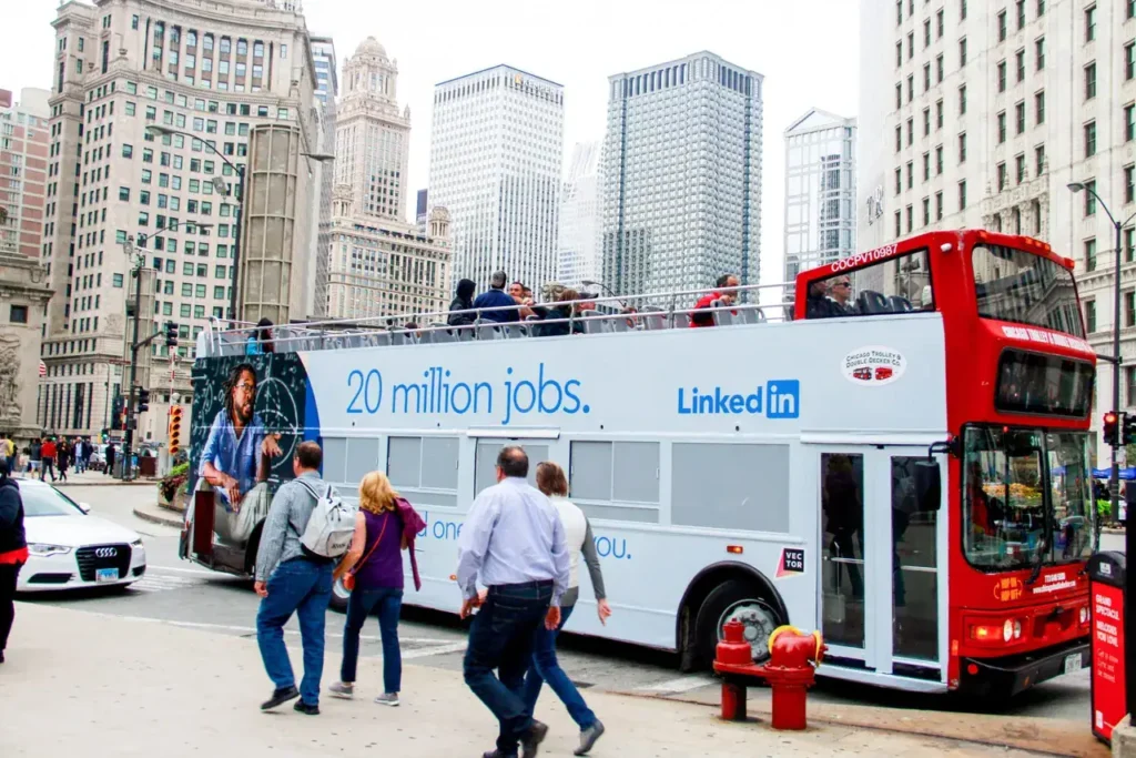 Double-decker bus featuring LinkedIn advertisement with "20 million jobs" slogan, urban setting with pedestrians and skyscrapers in background, illustrating bus advertising in transit marketing.