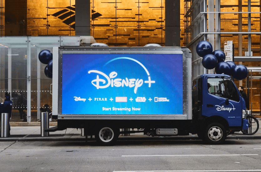 Disney+ advertisement on a truck showcasing streaming service, featuring logos of Disney, Pixar, Marvel, Star Wars, and National Geographic, with balloons, promoting brand visibility and audience engagement.