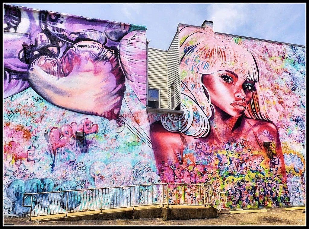 Colorful mural featuring a vibrant portrait of a woman with blonde hair and abstract designs, showcasing themes of love and creativity, relevant to mural advertising strategies in urban marketing.