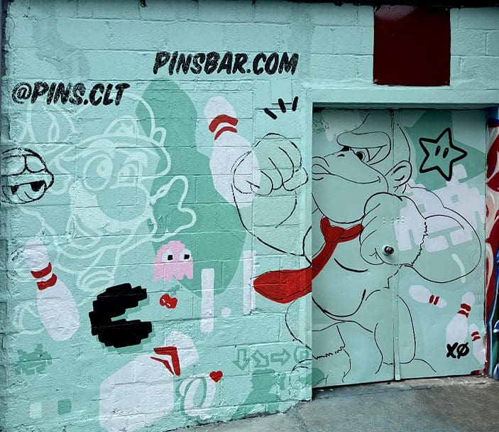 Mural featuring cartoon characters and gaming elements, including a character with a red tie, bowling pins, and playful designs, promoting Pins Bar with social media handles.
