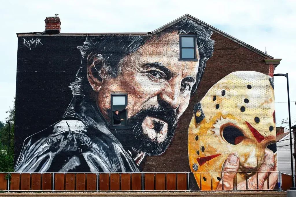 Mural featuring a dramatic portrait of a man with a beard alongside a hockey mask, illustrating guerrilla marketing in urban settings.