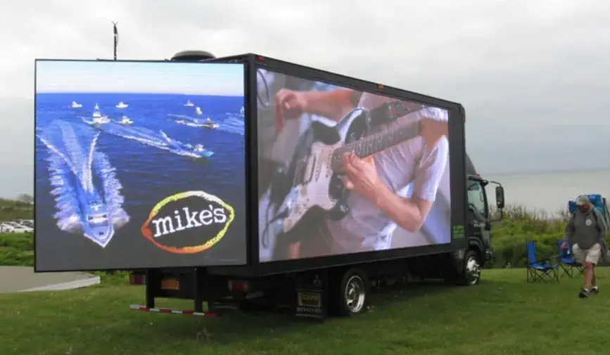Mobile advertising truck displaying vibrant digital screens featuring a boat and a guitarist, branded with "mike's," promoting guerrilla marketing strategies.