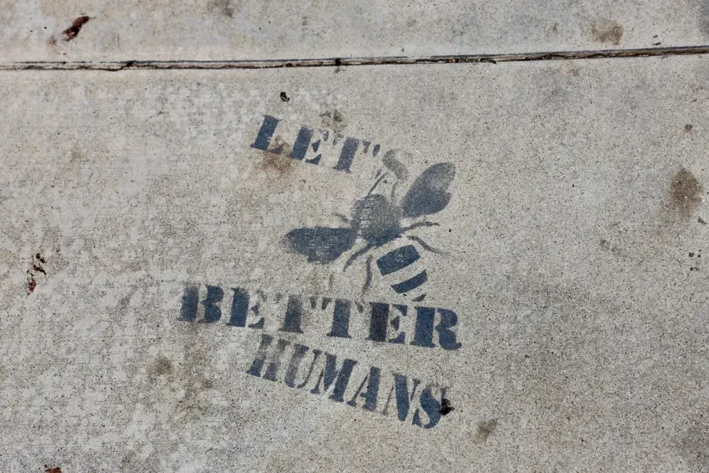 Sidewalk stencil featuring an ant and the text "LET'S BETTER HUMANS," emphasizing street advertising and community engagement in guerrilla marketing.
