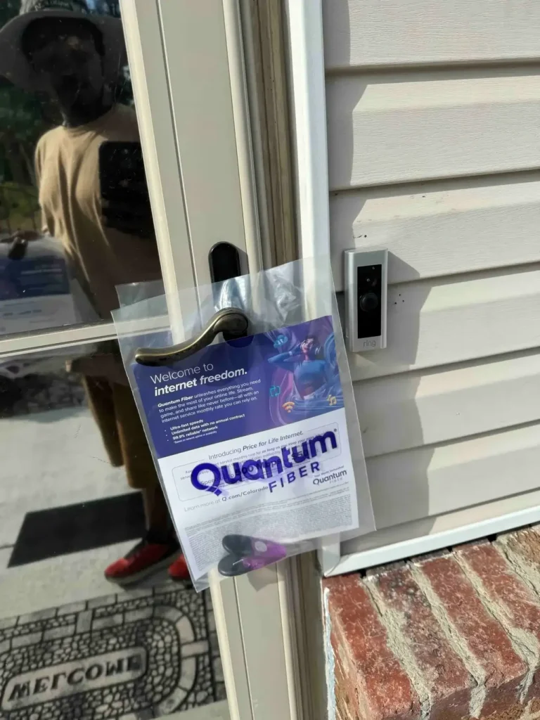 Door hanger advertising Quantum Fiber service, featuring promotional text about internet freedom, attached to a residential door with a doorbell visible.
