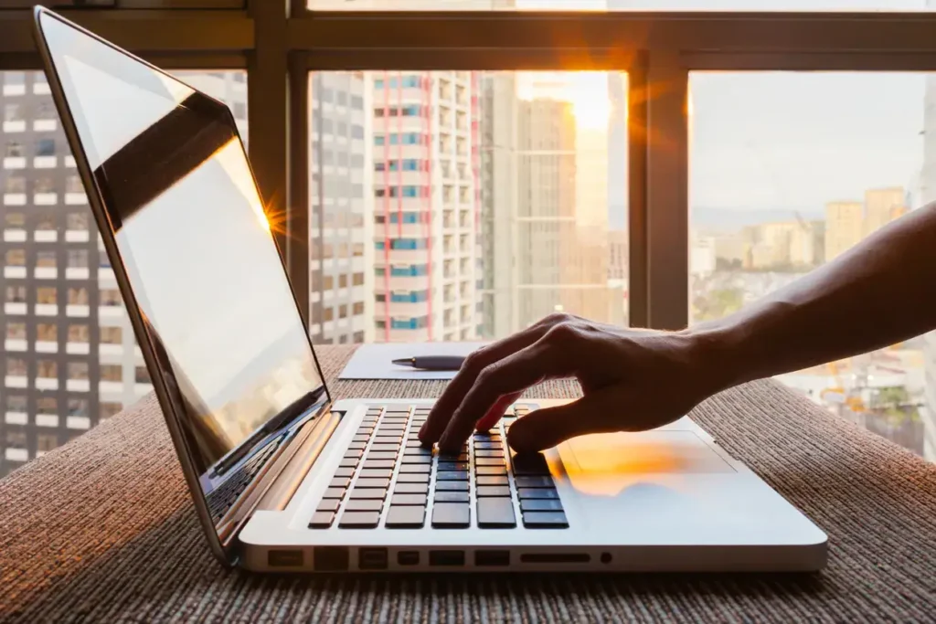 Person typing on a laptop with a city skyline in the background, reflecting a focus on content creation and social media strategies for enhanced brand visibility.