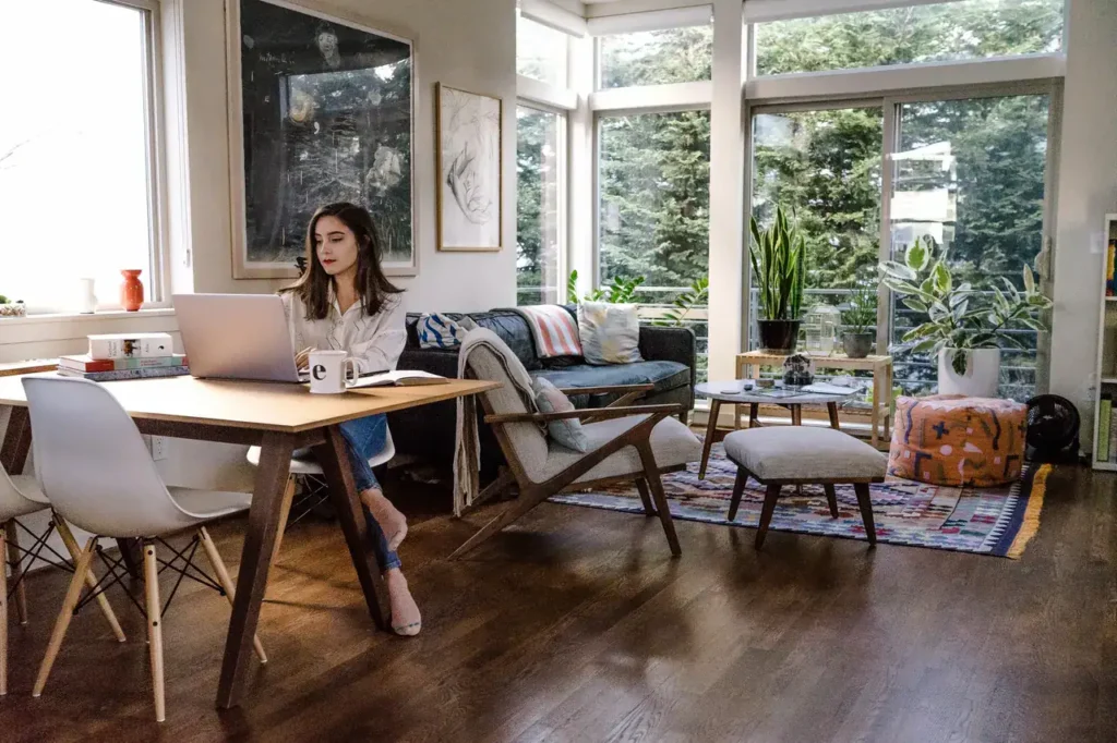 Woman working on a laptop at a modern home office table, surrounded by plants and natural light, illustrating content creation and remote work productivity.