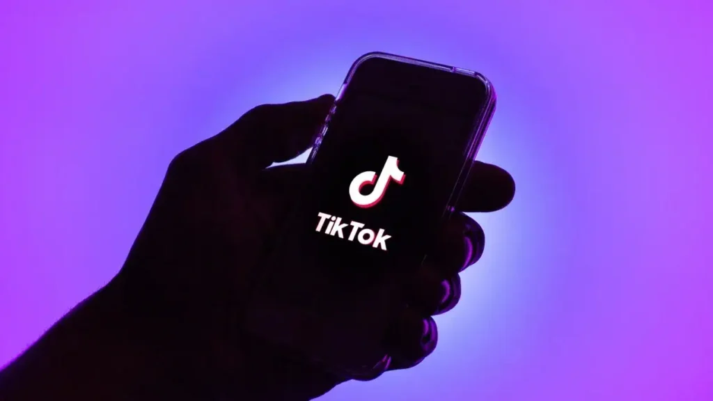 Hand holding smartphone displaying TikTok logo against a vibrant purple background, illustrating the impact of TikTok ads in digital marketing strategies.