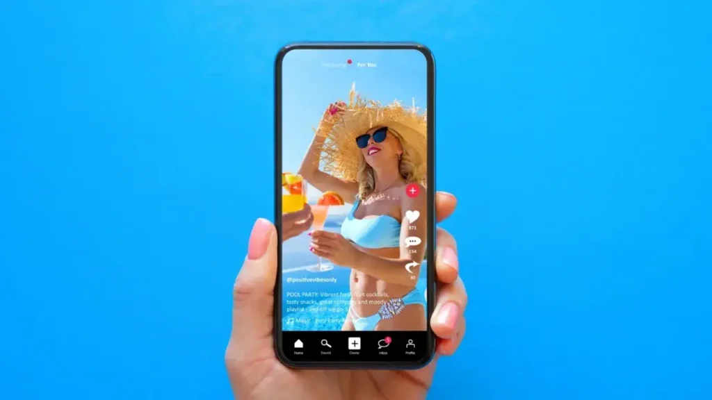 Hand holding smartphone displaying a vibrant TikTok video of a woman in a blue bikini and sunhat enjoying tropical drinks, emphasizing user engagement in digital marketing.