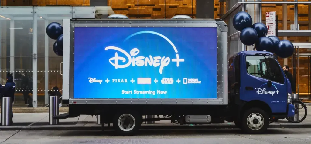 Disney+ promotional truck with large digital display advertising streaming services, featuring logos for Disney, Pixar, Marvel, and Star Wars, surrounded by blue balloons.