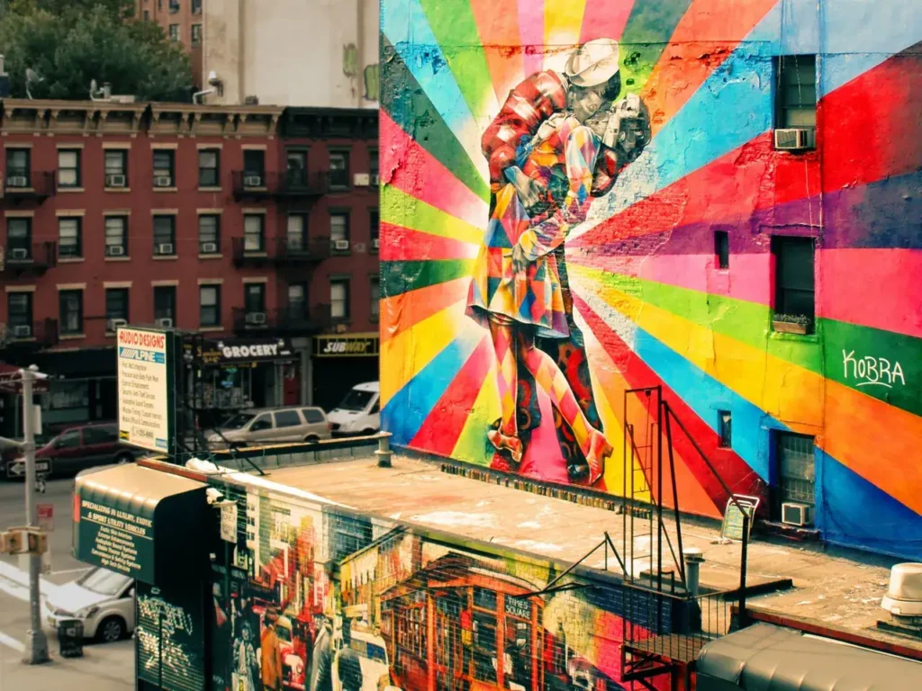 Colorful mural depicting a couple embracing, with vibrant rays radiating from the center, located on a building in an urban setting, emphasizing guerrilla marketing through street art.