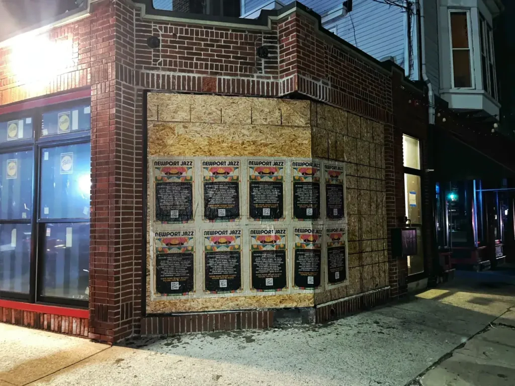 Posters promoting the Newport Jazz Festival displayed on a brick wall outside a bar, highlighting guerrilla marketing techniques in urban advertising.