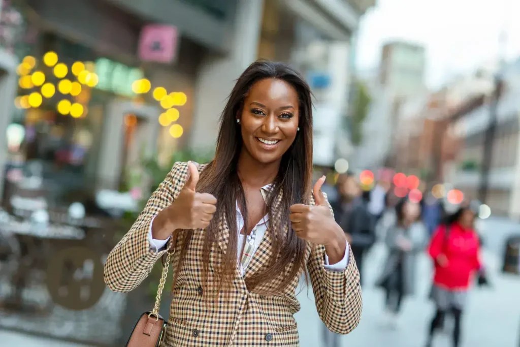 Smiling woman in a stylish blazer giving thumbs up in a vibrant urban setting, representing brand ambassadors' positive engagement in experiential marketing.