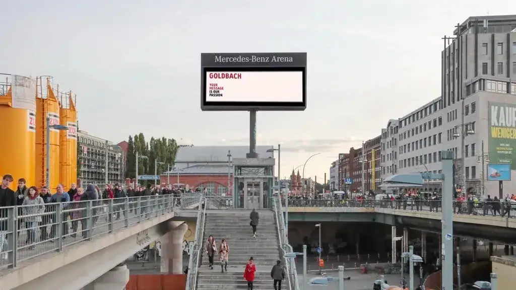 Billboard advertisement at Mercedes-Benz Arena, showcasing the brand "Goldbach" with pedestrians and urban scenery in a bustling city environment, highlighting media buying and guerrilla marketing strategies.