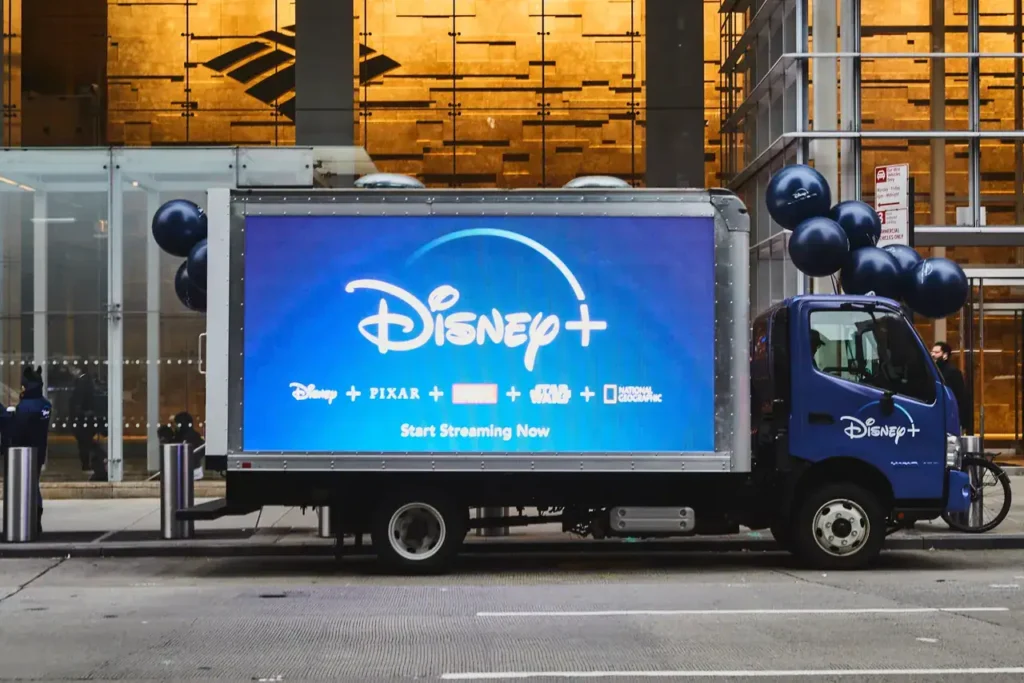 Disney+ advertising truck displaying promotional content, featuring the Disney+ logo and "Start Streaming Now" text, in an urban setting with balloons.
