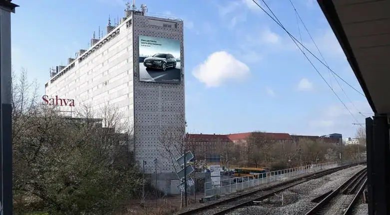 Billboard advertisement on a building featuring a car, with nearby railway tracks and trees, emphasizing urban advertising strategies for international markets.