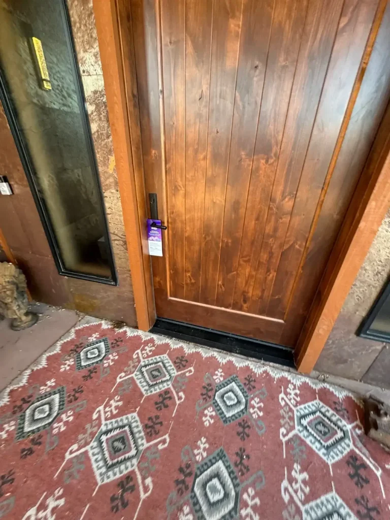 Wooden front door with a door hanger promotion attached, set against a patterned rug and stone wall, illustrating door hanger marketing strategies in local advertising.