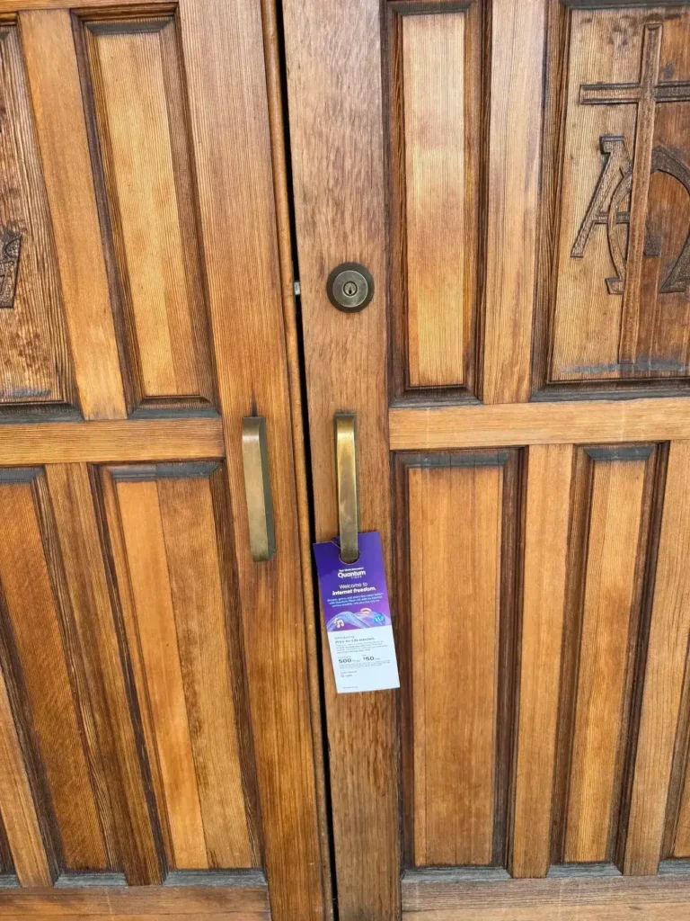 Wooden double doors with a promotional door hanger featuring a welcome message and details about internet services, emphasizing hyperlocal marketing strategies.