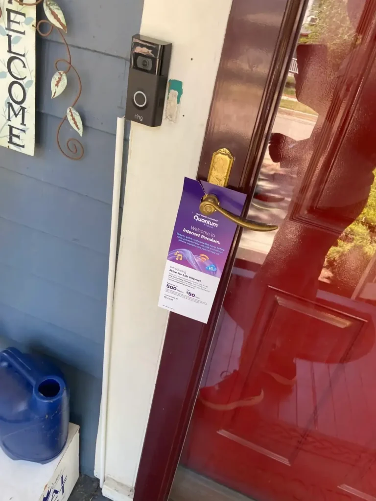 Door hanger promotion featuring a colorful advertisement for a service, attached to a door handle, with a Ring doorbell visible, showcasing hyperlocal marketing strategies.