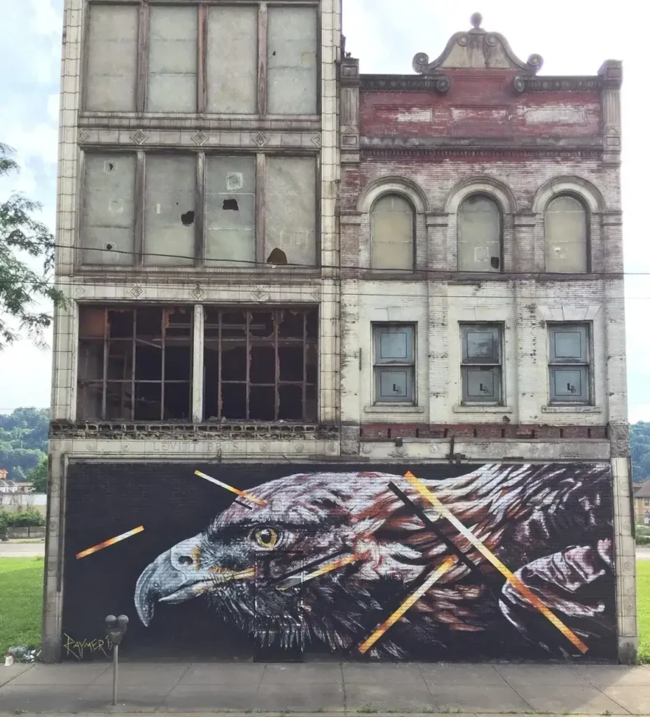 Mural of a hawk on a dilapidated building, showcasing urban art and guerrilla marketing techniques.