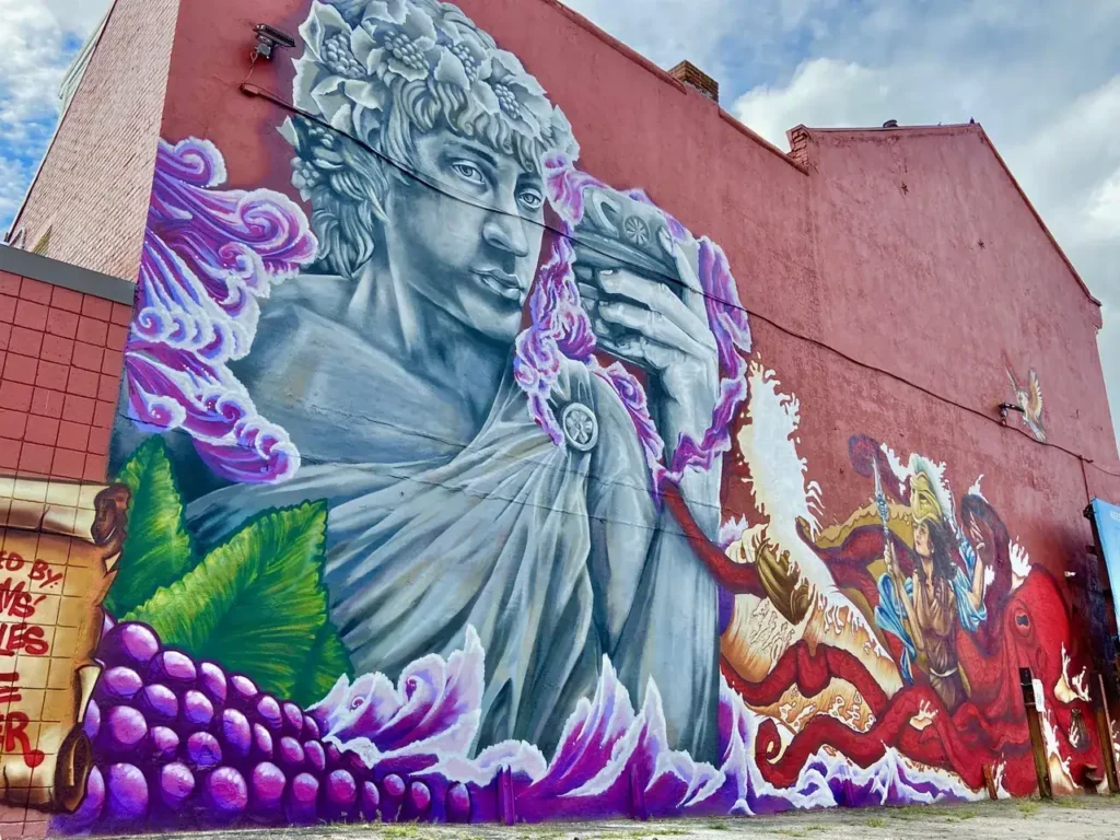 Mural featuring a classical figure holding a cup, surrounded by grapes and vibrant colors, illustrating urban mural advertising strategies relevant to guerrilla marketing campaigns.