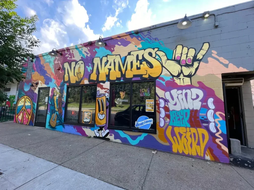 Colorful mural on building exterior featuring the text "NO NAMES," peace symbol, and graffiti-style art, representing urban mural advertising in New York City.