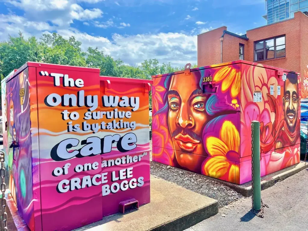 Mural featuring vibrant portraits and a quote by Grace Lee Boggs, emphasizing community care, in an urban setting related to guerrilla marketing strategies.