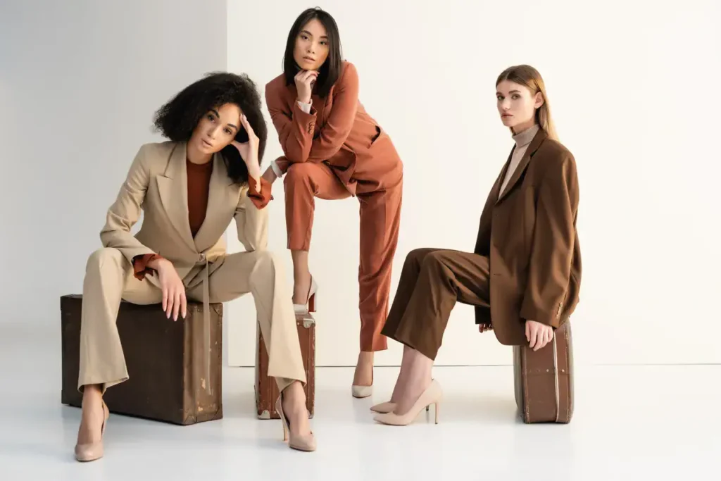 Three women in stylish suits posing on vintage suitcases, showcasing modern fashion for professional events and marketing.