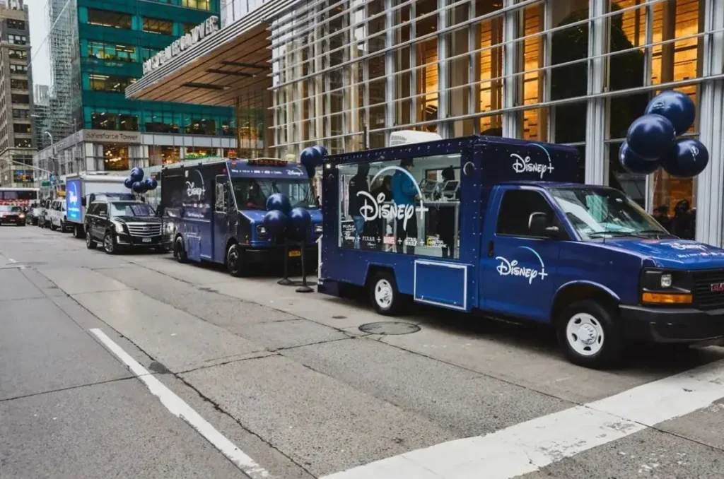 Mobile showrooms featuring Disney+ branding, parked on a city street, with promotional balloons and advertising displays, showcasing innovative guerrilla marketing strategies.