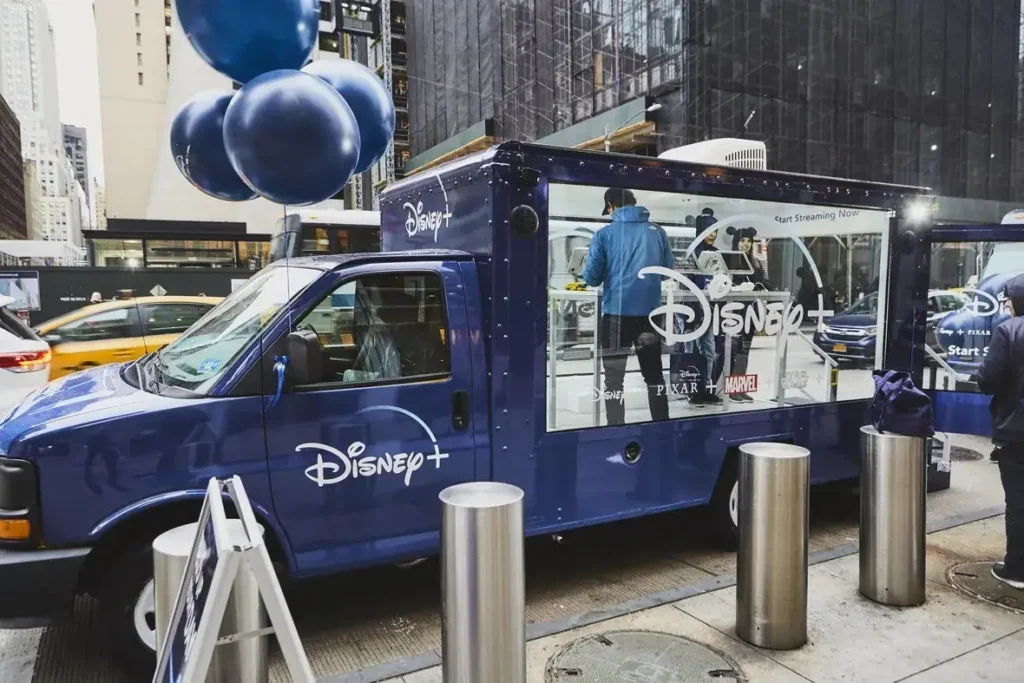 Disney+ promotional van in urban setting with staff engaging customers, showcasing brand activation and experiential marketing strategies.