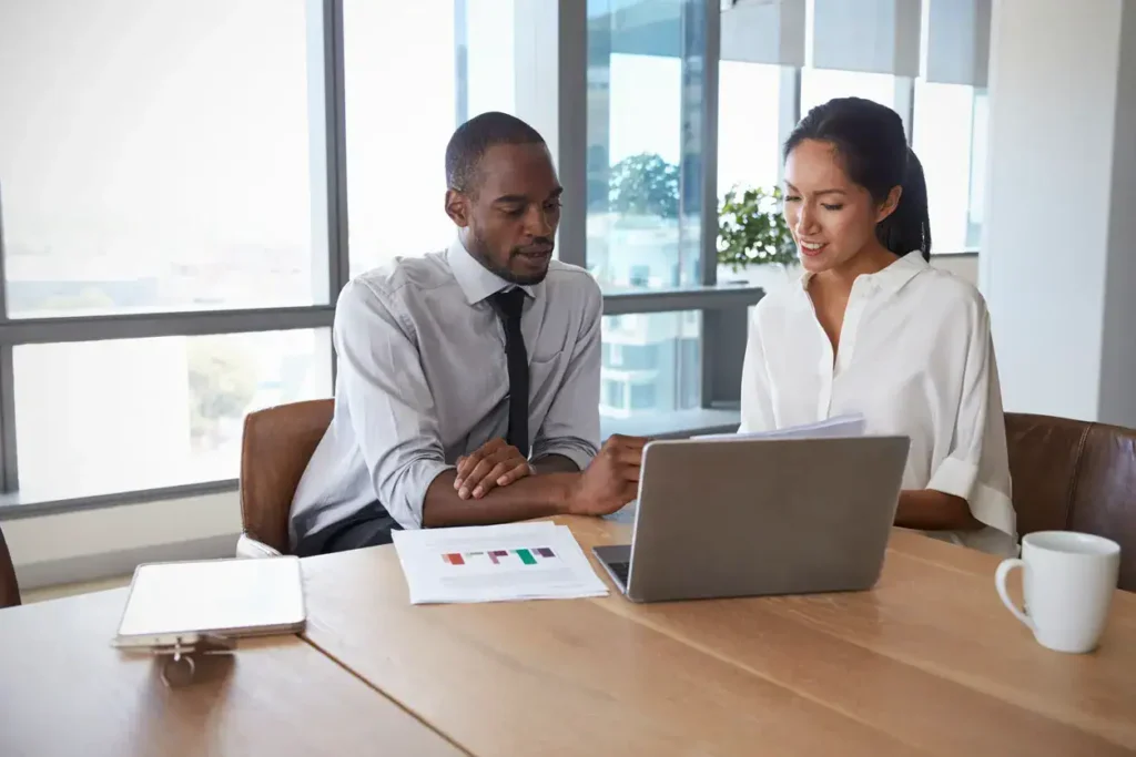 Business professionals collaborating over a laptop in a modern office, discussing marketing strategies and brand ambassador services.
