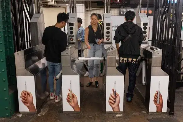Subway turnstiles with advertising featuring hands holding a pen, showcasing innovative marketing strategies in transit advertising.