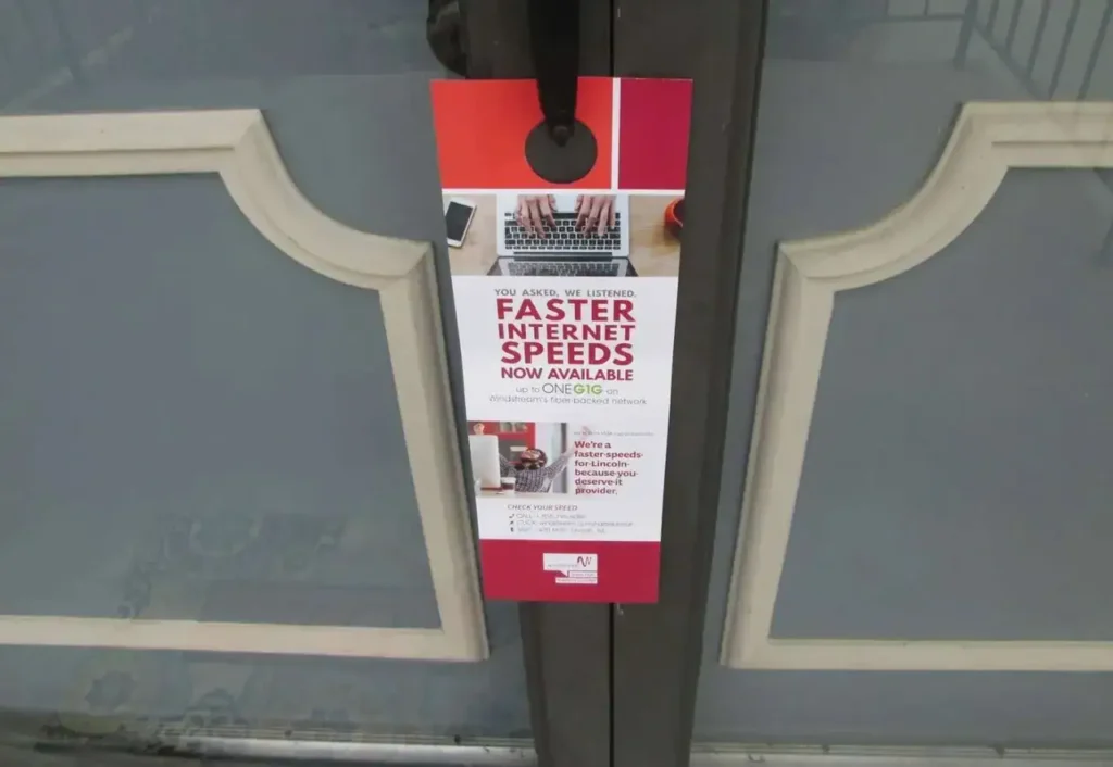 Door hanger advertising promoting faster internet speeds, featuring a laptop and text highlighting "Faster Internet Speeds Now Available One Gig" and contact information, relevant to guerrilla marketing strategies.